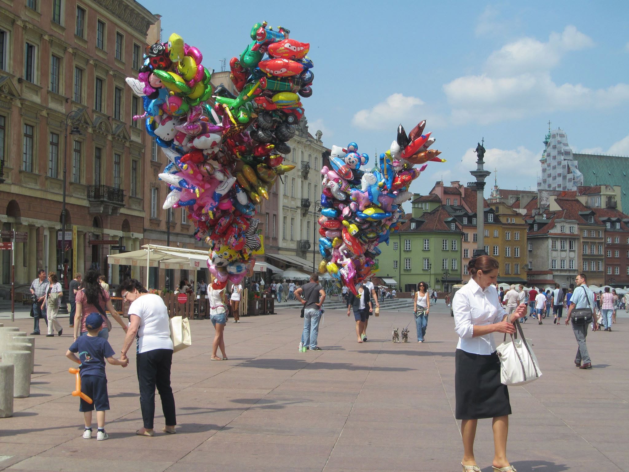 People walking through a city square among colourful balloon displays.